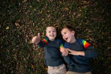 Two happy boys laying in leaves during a family lifestyle photoshoot in Trophy Club Keller Flower Mound Texas with international award winning photographer